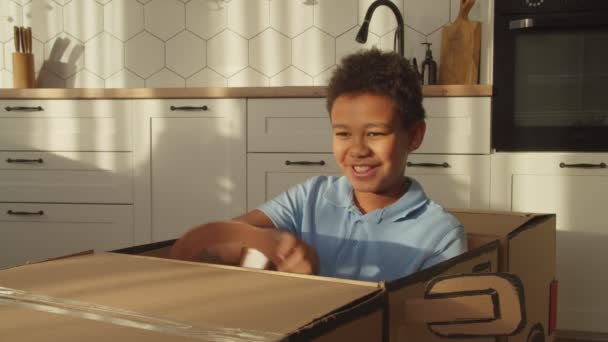 Retrato de niño negro preadolescente despreocupado jugando, conduciendo coche de cartón de juguete — Vídeos de Stock