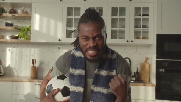 Emocional fanático del fútbol masculino negro con pelota de fútbol celebrando gol en casa — Vídeo de stock