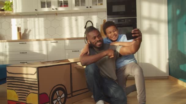 Alegre Africano pai e filho tomando selfie na frente de diy brinquedo carro de papelão — Vídeo de Stock