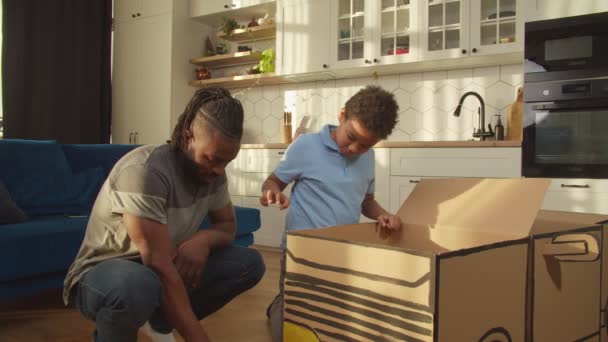 Leuke Afro-Amerikaanse zoon en vader spelen met speelgoed kartonnen auto thuis — Stockvideo