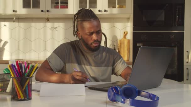 Fokuserad afrikansk man med bärbar dator gör hem redovisning rutin hemma — Stockvideo