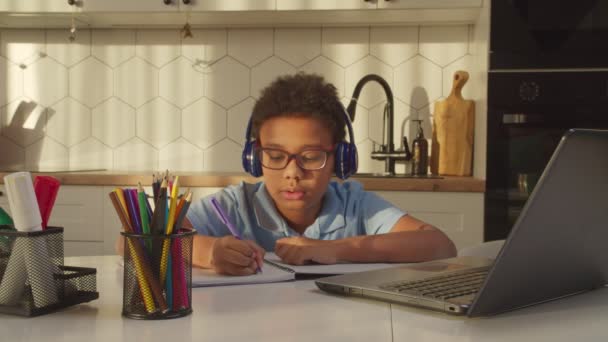 Inteligente colegial negro en auriculares e-learning usando ordenador portátil PC en casa — Vídeos de Stock