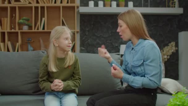 Симпатичная дочка школьного возраста с нарушением слуха и мать делят и склеивают на диване — стоковое видео
