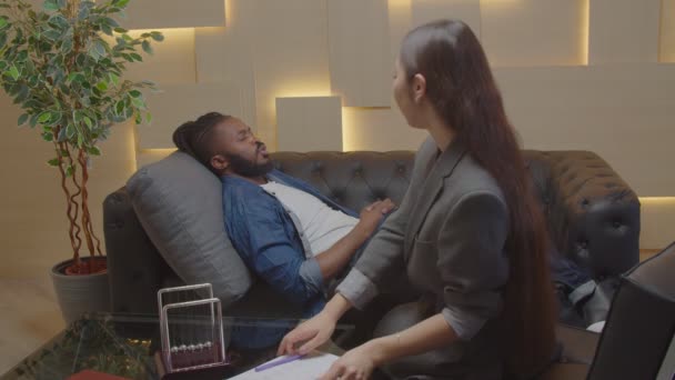 Aziatisch vrouw psycholoog wakker gestresst zwart man van hypnose binnen — Stockvideo