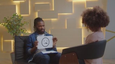 Afrikalı erkek psikolog duygusal kartlar kullanarak çocukla psikoterapi yapıyor.