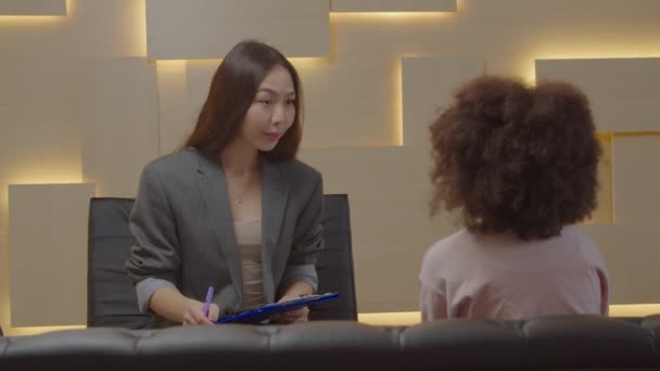 Aziatische vrouw sociaal werker werken met weinig zwart meisje met sociaal fobie — Stockvideo