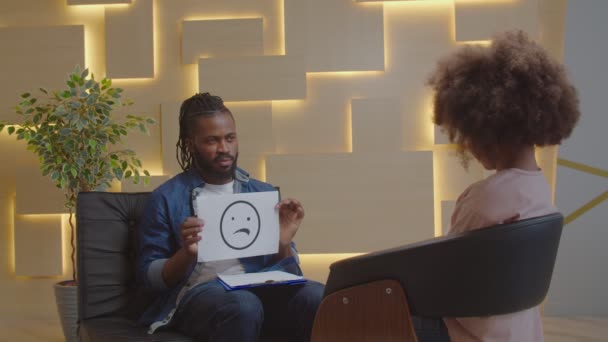 Afrikanischer männlicher Psychologe macht Psychotherapie mit Kind mittels Emotionskarten — Stockvideo