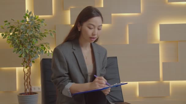 Азійська жінка-психотерапевт, яка працює з пацієнтом і робить нотатки — стокове відео