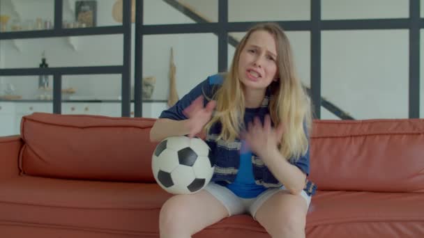 魅力的な中年女性サッカーサポーターでスポーツジャージーでボールとスカーフテレビでサッカーゲームを見て 感情的にゴールミスに反応し 失望と迷惑を表現屋内 — ストック動画