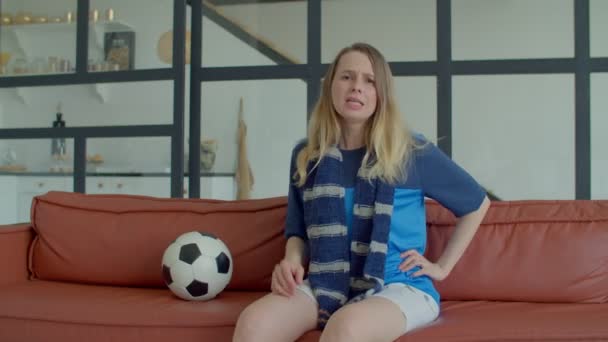 完全にゲーム魅力的な中年女性ファンでスポーツジャージーでサッカースカーフとボールはテレビでサッカー試合を見ます 家でソファに座っている間 感情的に応援チーム — ストック動画