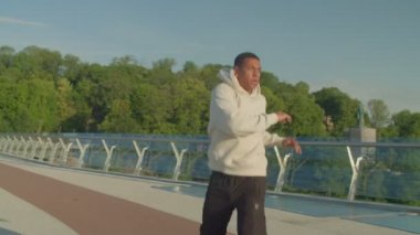 Aktif motivasyonlu sportif formda Afro-Amerikan bir adam ısınıyor ve kaslarını kasıyor. Sabah koşusuna hazırlanıyor. Şehir caddesinde güneş ışığının altında spor antrenmanı yapıyor..