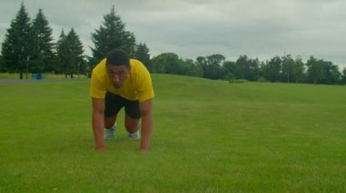 Etkin motivasyonlu sportif formda Afro-Amerikan erkek, yan ayı emekleme egzersizi yapıyor, çekirdek gücünü geliştiriyor, parkta yeşil alanda çalışırken denge ve omuz kaslarını geliştiriyor..