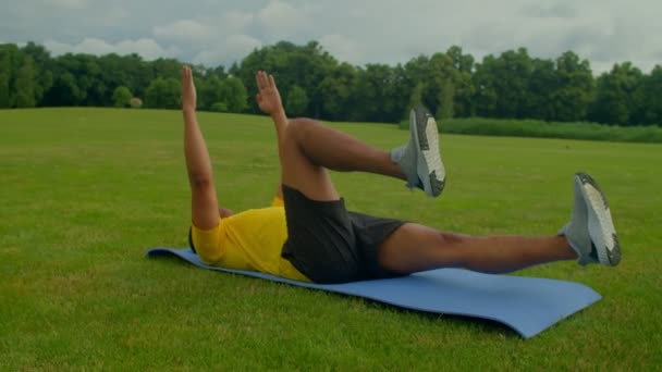 フィットネスマットの上に横たわるアフリカ系アメリカ人男性のアクティブなスポーティフィットを決定し 公園でのトレーニング中にコア 背中の筋肉の強化と安定化 — ストック動画