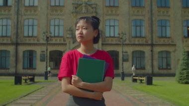 Portrait of depressed emotionally stressed pretty Asian female student with textbooks walking at campus after failed university exam, expressing disappointment and anxiety.