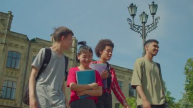 Portrait of happy carefree diverse multicultural students with textbooks and backpacks walking after study at university campus, friendly chatting and sharing, expressing happiness and positivity.