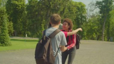 Group of excited diverse multicultural college friends with backpacks embracing, greeting each other with high five, expressing positivity and happiness while meeting at campus after summer holidays.