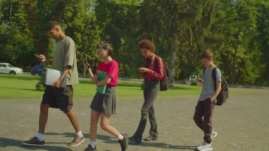 Busy with cellphones diverse multiethnic college students walking to university lecture at campus, networking and browsing social media content online, phubbing each other.