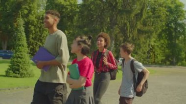 Neşeli, güzel, çok kültürlü, çok kültürlü üniversite arkadaşları ders kitapları ve sırt çantalarıyla arkadaşça konuşuyor ve paylaşıyorlar. Üniversite kampüsünde okumak için yürürken mutluluk ve pozitifliği ifade ediyorlar..