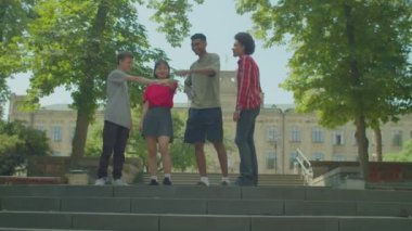 Cheerful handsome diverse multiracial college students making pile of hands, expressing strong friendship, togetherness, trust and cooperation while standing outside university building.