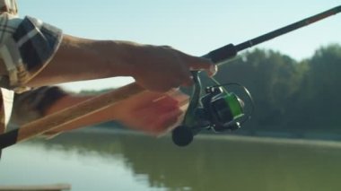 Relaxed attractive African American man casting spin fishing rod, enjoying recreational activity and freshwater fishing on pond at daybreak while spending leisure during summer vacation.