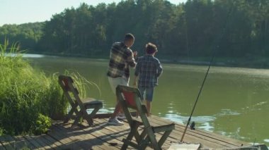 Upset cute preadolescent boy and handsome African American father fishing together with spin fishing rod, expressing disappointment by fish got away while multiracial family relaxing on lake.