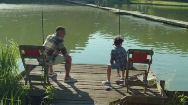 Joyful cute preadolescent Middle Eastern son and handsome black father catching fish on fishing rod, expressing excitement and happiness while multiethnic family enjoying fishing on lake at sunrise.