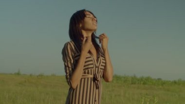 Side view of beautiful African American woman with eyes closed inhaling deeply and enjoying fresh air, expressing happiness and positive vibes while relaxing in countryside at dawn.