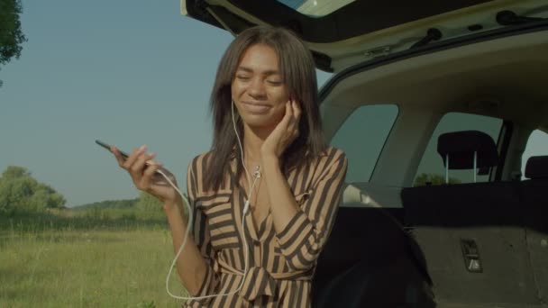 Carefree Attractive Black Female Traveler Sitting Car Trunk Listening Music — Stockvideo