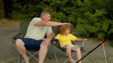 Yakışıklı bir babanın portresi ve güzel kızıl saçlı bir oğlun nehir kıyısında oltalarla oturup manzaralı doğal manzaraya bakması ve gölette dinlenirken balık tutmayı tartışması..