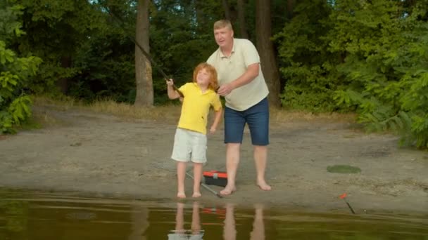 关爱的父亲教可爱的红头发学龄儿童钓鱼技巧 一起抛出钓竿 为成功欢呼 而快乐的家庭则享受着闲暇和湖上的垂钓 — 图库视频影像