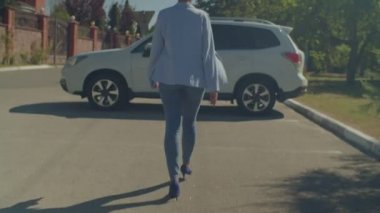 Yüksek topuklu ayakkabılar giyen, şık kıyafetler giyen, otoparkta yürüyen ve iş toplantısından sonra arabaya binen başarılı Afrikalı Amerikalı iş kadını. .