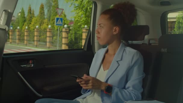 不耐烦而又漂亮的黑人女企业家 她坐在汽车后座上 一边看手表 一边迟到 还叫司机赶时间 这一切都让她烦躁不安 — 图库视频影像