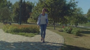 Yüksek topuklu ayakkabılar giyen, iş kıyafetleri giyen, elinde belgeler ve dijital tablet tutan, iş günü parkı boyunca yürüyen, kendine güvenen, zarif, çekici, siyah kadın girişimci..