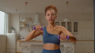 Motive olmuş güzel aktif spor formundaki Afro-Amerikan kadın ağırlık antrenmanı yapıyor, dambıl önünde yükseltiyor, vücut gücünü arttırıyor, omuz hareketliliğini ve istikrarını geliştiriyor..