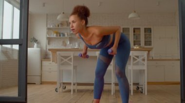 Odaklanmış motive edici çekici spor formundaki Afrikalı kadın ağırlık antrenmanı yapıyor, dambıl sırtına eğiliyor, belinin üst ve alt kısmını güçlendiriyor, kalça kasları, bacak ve omuzları güçlendiriyor..