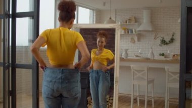 Neşeli, pozitif, bol kotlu Afro-Amerikan kadın, aynadaki yansımaya bakıyor, başarılı kilo verme diyetini gösteriyor ve iç mekandaki vücut şekillerine hayran..