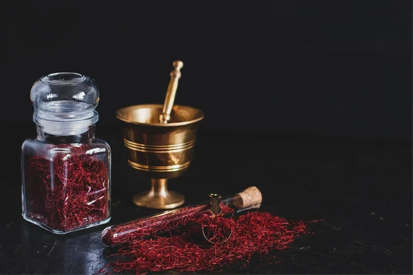 Rohes, rot getrocknetes Safran-Gewürz auf Holzgrund in Vintage-Messingmörtel mit Stößel, Glas und Rohr — Stockfoto