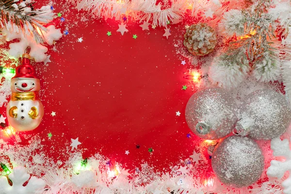 Luces navideñas bordean con adornos y nieve sobre fondo rojo — Foto de Stock