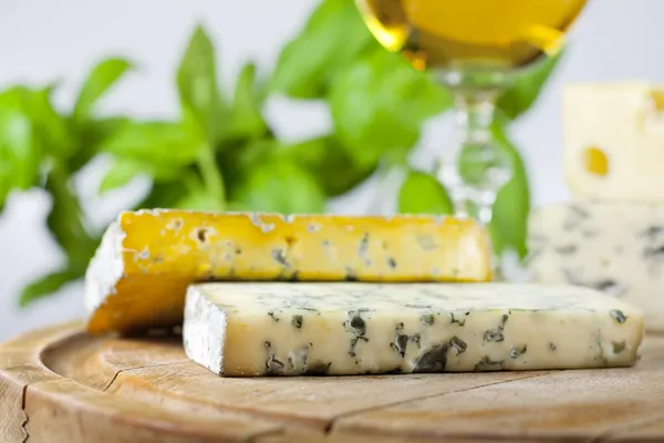 Cheese on cutting board closeup with basil and wine — Stock Photo, Image