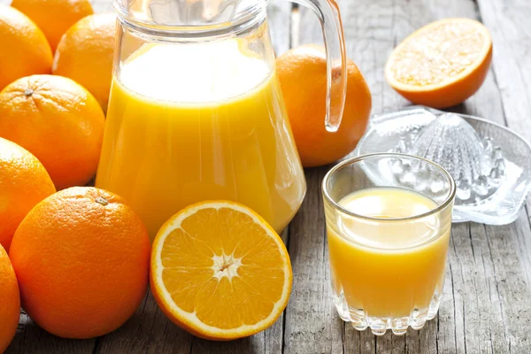 Orangensaft mit Quetsche und Kanne auf Holzbrettern — Stockfoto