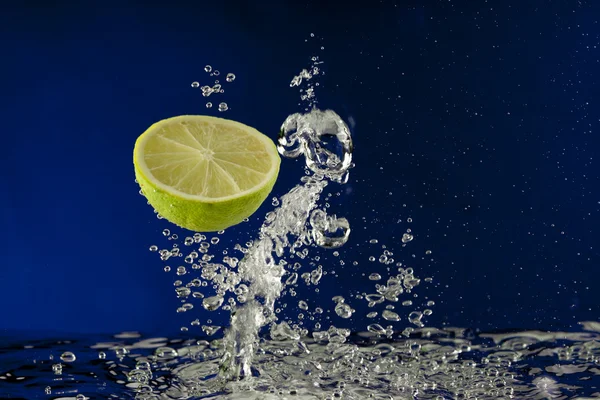 Fruit lime splash in water with bubbles against blue background Stock Image
