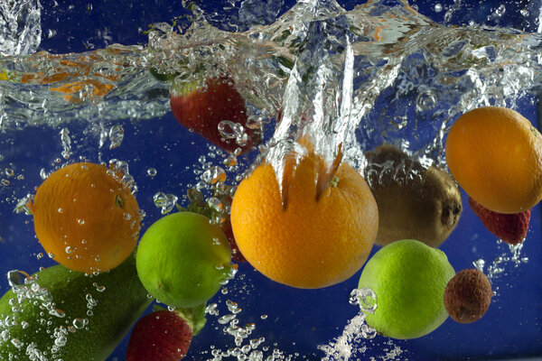 Fruits splash in water with bubbles against blue background