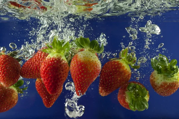 Strawberry splash in water with bubbles against blue background — Stock Photo, Image