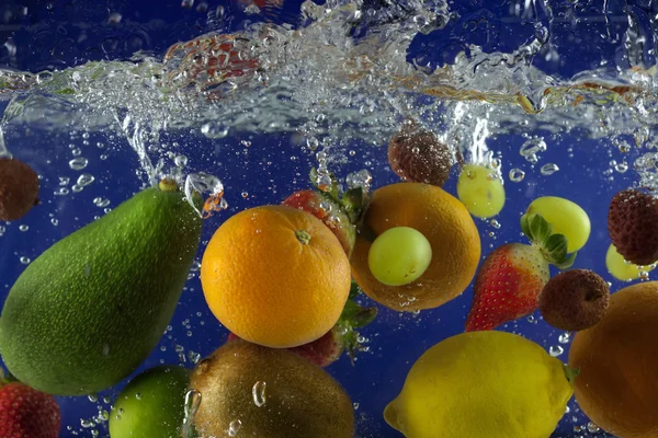 Fruits éclaboussent dans l'eau avec des bulles sur fond bleu — Photo