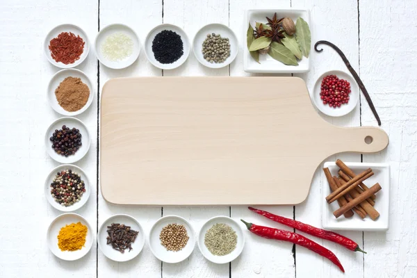 Kryddor och torkade grönsaker med skärbräda på vita plankor Stockfoto