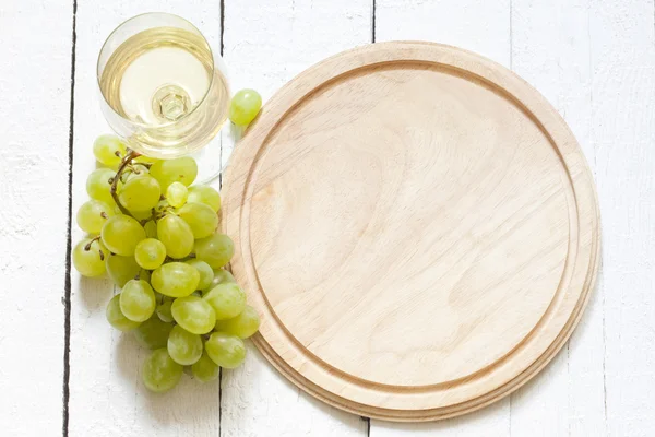 Glass of wine and grapes with empty cutting board background — Stock Photo, Image