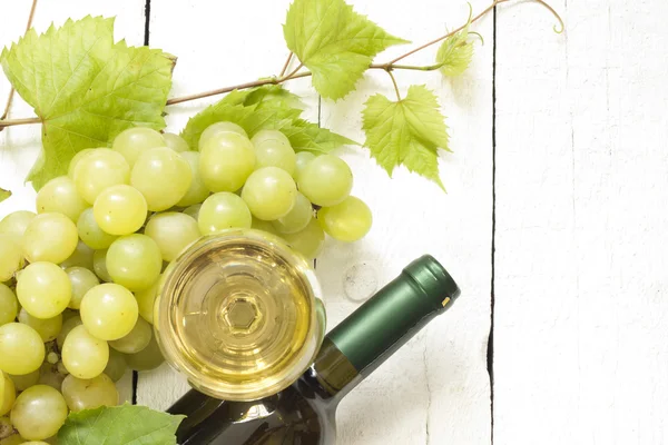 Glass of white wine with bottle and grapes on vintage boards — Stock Photo, Image