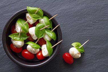 Caprese peynirli, domatesli ve fesleğenli çubuklar siyah arka planda kasede.