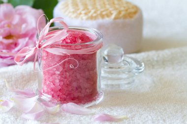 Cam şişede gül banyosu tuzu, vücut bakım aksesuarları ve arka planda taze gül yaprakları, spa konsepti.