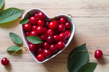 Tahta zemin üzerinde kalp şeklinde bir kasede taze kiraz meyveleri.